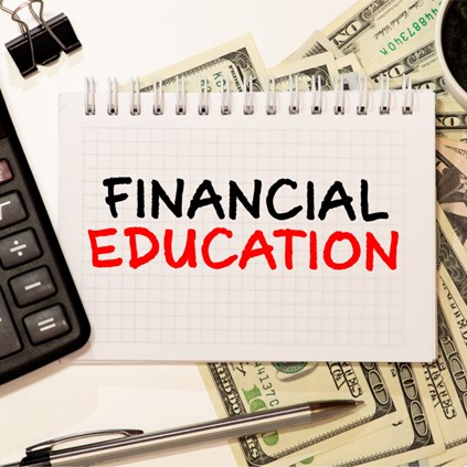 Financial Education on spiral notes with dollar notes in background, laptop, pen, clip on table